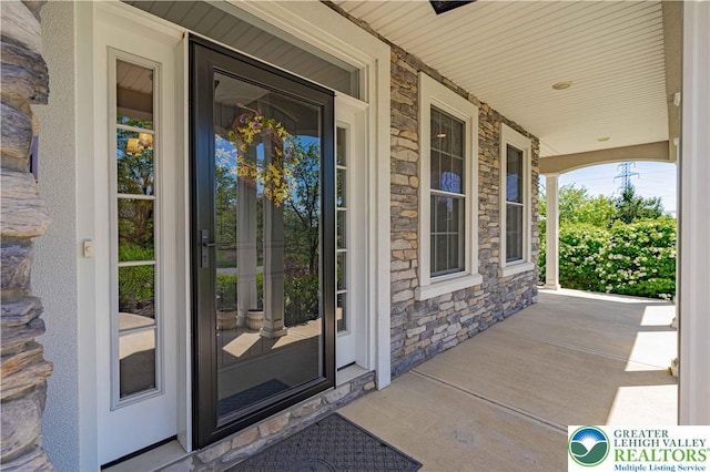 doorway to property with stone siding and covered porch