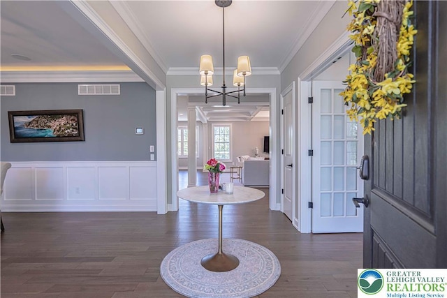 entrance foyer featuring dark wood-type flooring, ornamental molding, a chandelier, wainscoting, and a decorative wall