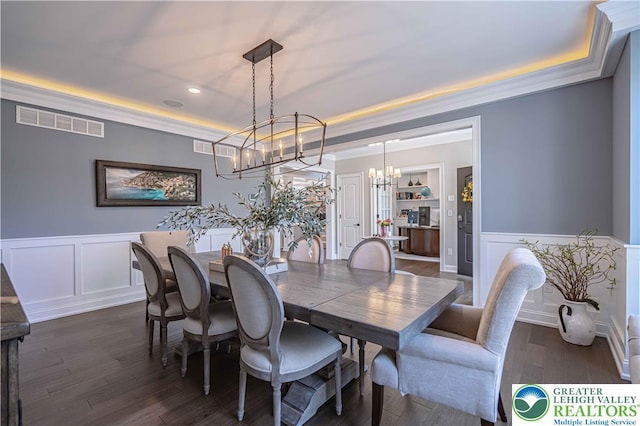 dining area featuring a raised ceiling, a chandelier, a decorative wall, a wainscoted wall, and dark wood finished floors