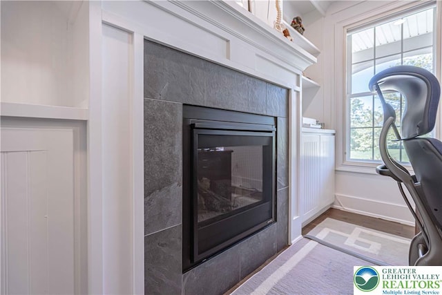 detailed view of wood finished floors, a tile fireplace, and baseboards