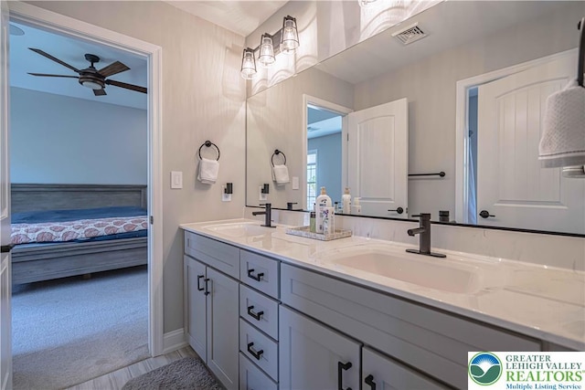ensuite bathroom featuring ceiling fan, double vanity, and baseboards