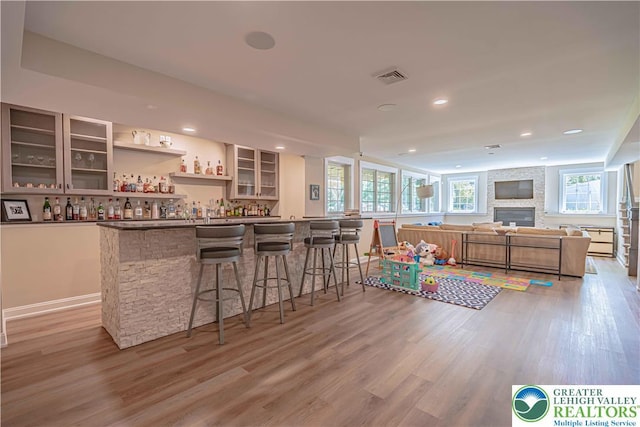 indoor bar with light wood-type flooring, recessed lighting, and a fireplace