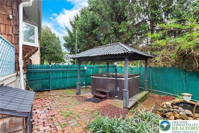 view of patio with a hot tub, a fenced backyard, and a gazebo