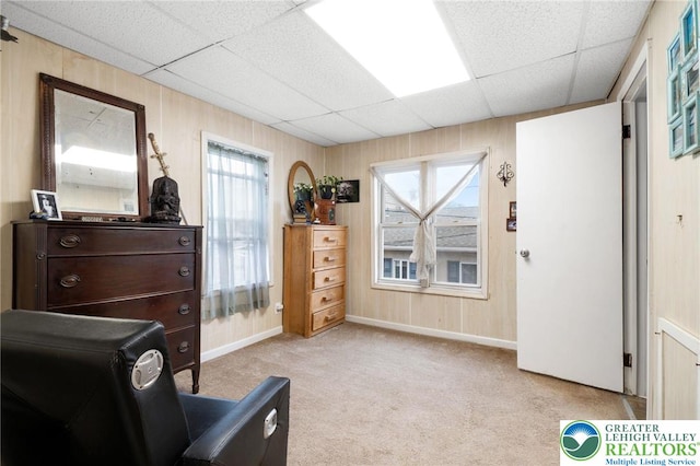 bedroom featuring light carpet, a paneled ceiling, baseboards, multiple windows, and wooden walls