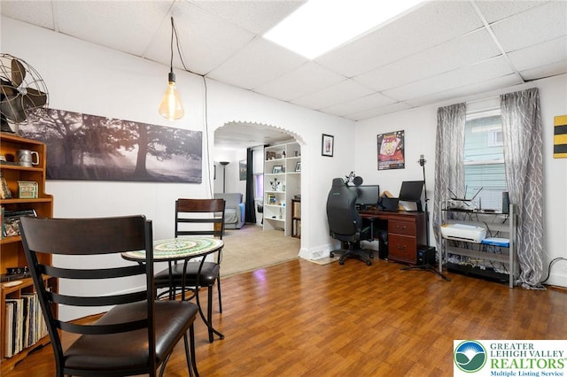 dining room with a drop ceiling, arched walkways, wood finished floors, and an office area