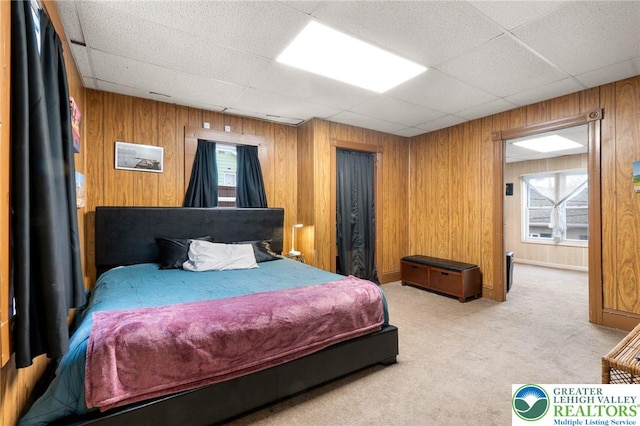 carpeted bedroom featuring a paneled ceiling, wood walls, and multiple windows