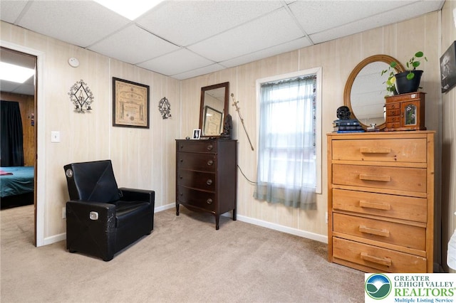 living area with a drop ceiling, carpet, and baseboards