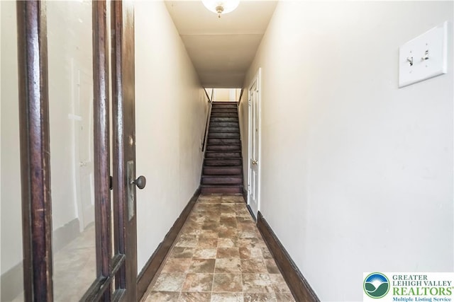 hall with stone finish floors, baseboards, and stairs