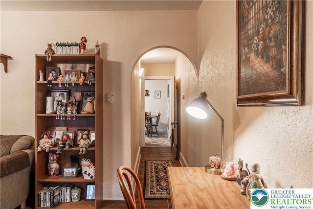 dining area featuring arched walkways, a textured wall, and wood finished floors
