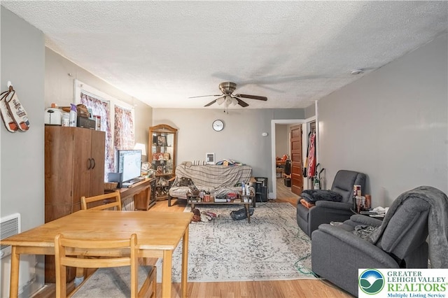 living room featuring light wood-type flooring, ceiling fan, and a textured ceiling