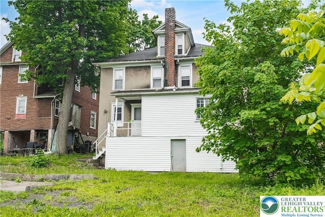 back of property featuring a chimney and a lawn