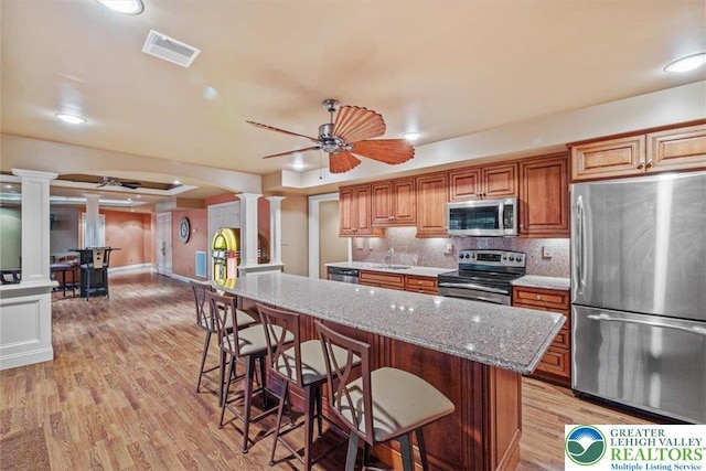 217 Rising Meadow Way, Middle Smithfield Twp, PA 18302 - kitchen featuring stainless steel appliances, ornate columns, light wood-type flooring, a kitchen breakfast bar, and decorative backsplash