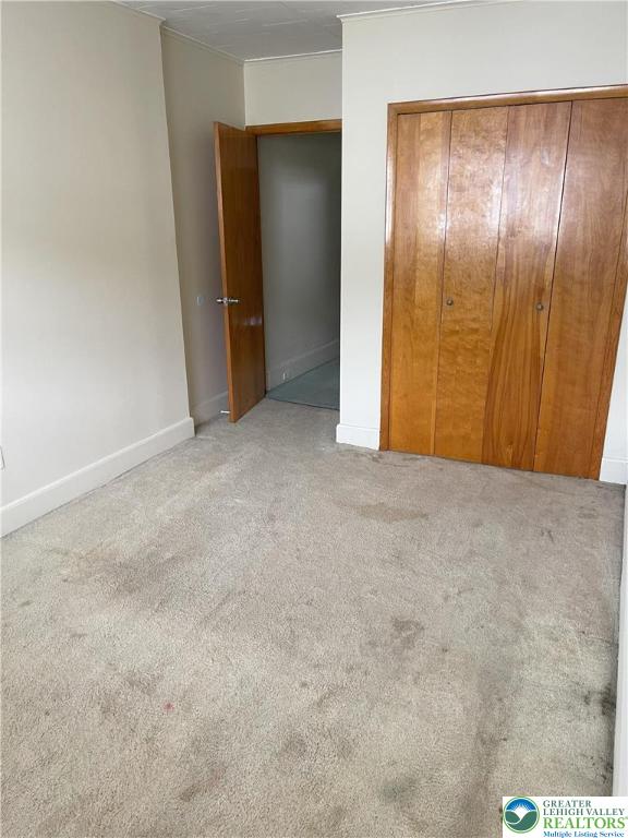 unfurnished bedroom with carpet flooring, a closet, ornamental molding, and baseboards