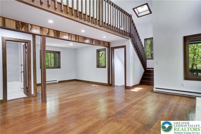 8210 Pine Grove, Stroud Twp, PA 18301 - unfurnished living room with baseboard heating, healthy amount of natural light, wood finished floors, a towering ceiling, and stairway