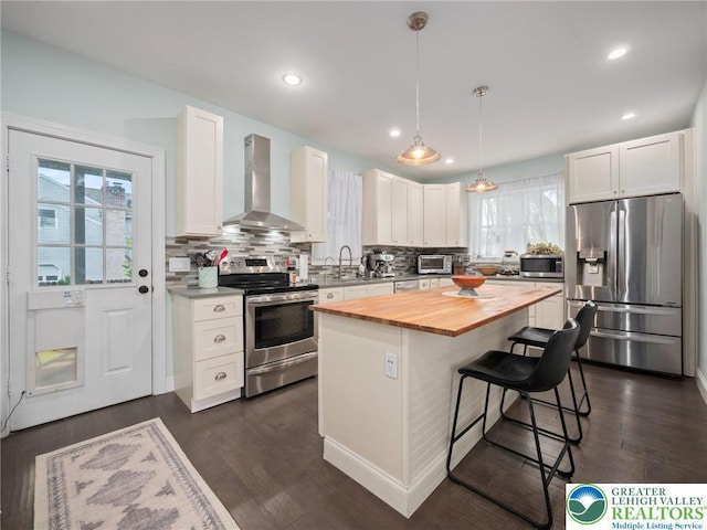 kitchen featuring stainless steel appliances, wall chimney exhaust hood, wooden counters, a breakfast bar area, and backsplash