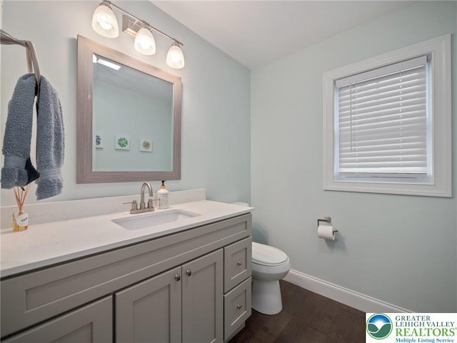 bathroom with baseboards, wood finished floors, vanity, and toilet