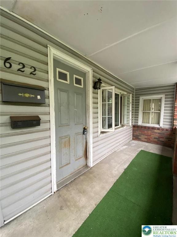 doorway to property featuring covered porch and brick siding