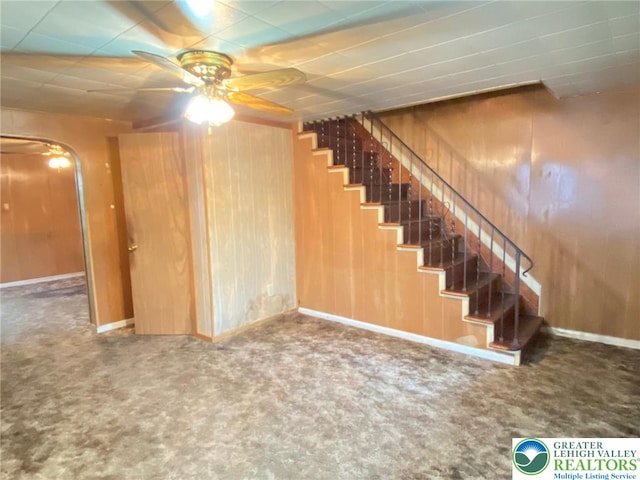 staircase featuring ceiling fan, carpet flooring, and wood walls