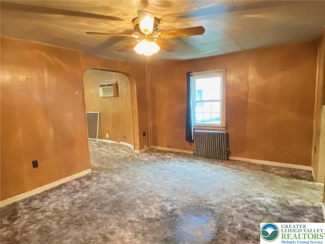 empty room featuring radiator, a ceiling fan, arched walkways, carpet floors, and baseboards