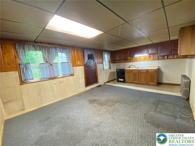 kitchen featuring radiator heating unit, a paneled ceiling, baseboards, brown cabinetry, and wood walls