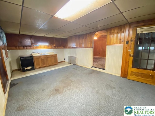 below grade area featuring a paneled ceiling, carpet, arched walkways, wood walls, and baseboards