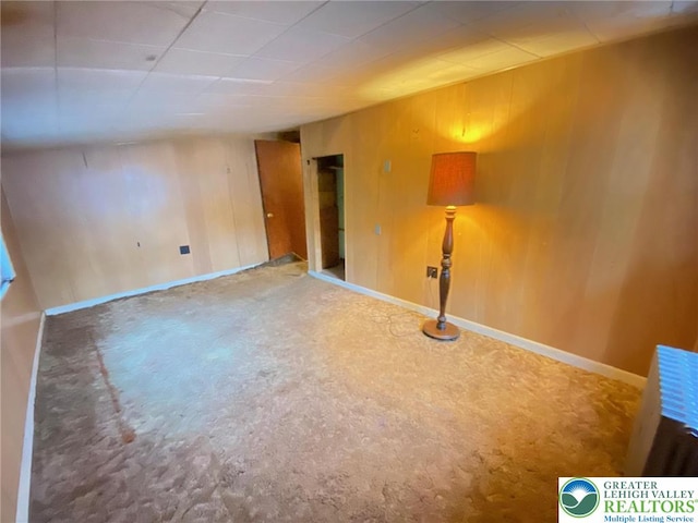 carpeted spare room featuring wood walls and baseboards