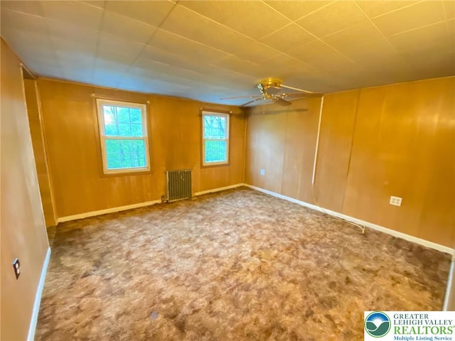 carpeted empty room with radiator, a ceiling fan, and baseboards
