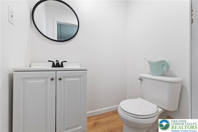half bath with wood finished floors, vanity, toilet, and baseboards