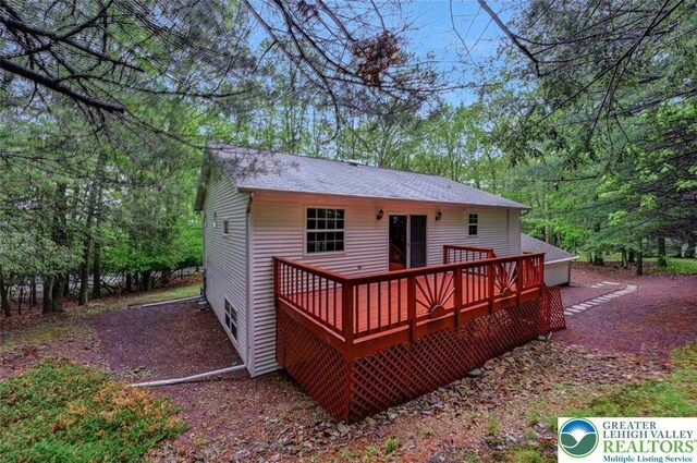 back of house featuring a wooden deck and roof with shingles