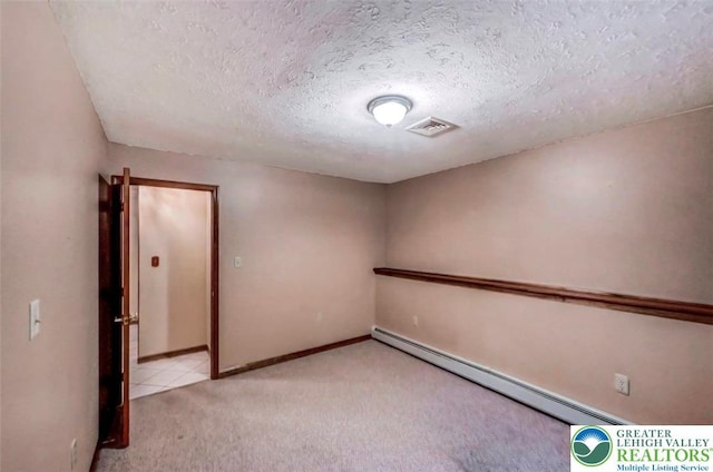 spare room featuring a baseboard heating unit, light colored carpet, a textured ceiling, and baseboards