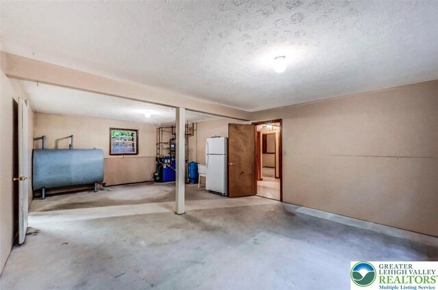 finished basement featuring freestanding refrigerator, oil tank, a textured ceiling, and a heating unit