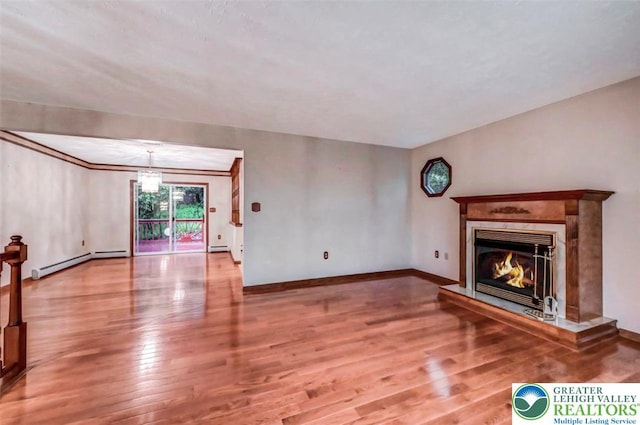unfurnished living room with a baseboard heating unit, wood finished floors, a glass covered fireplace, and baseboards
