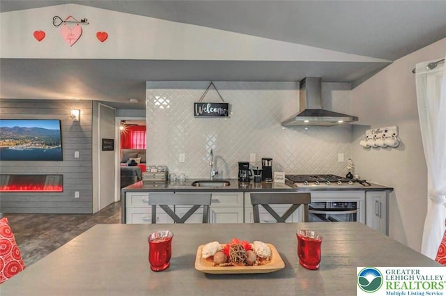 304 Ruger Ln, Coolbaugh Twp, PA 18466 - kitchen featuring wall chimney range hood, appliances with stainless steel finishes, lofted ceiling, a large fireplace, and dark countertops