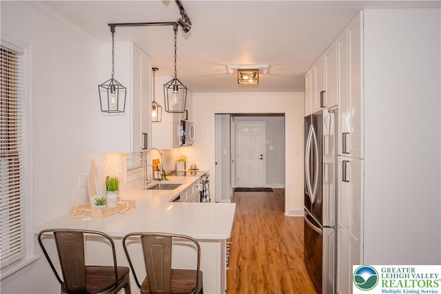 kitchen featuring appliances with stainless steel finishes, white cabinets, light countertops, a peninsula, and light wood finished floors