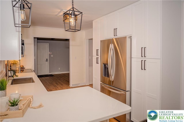 kitchen with stainless steel fridge, light countertops, white cabinetry, wood finished floors, and a sink