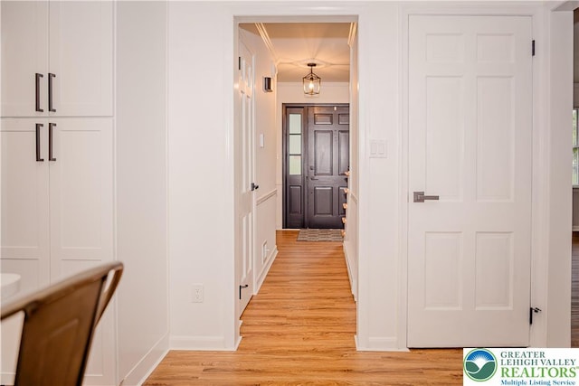 hall with light wood finished floors, crown molding, and baseboards