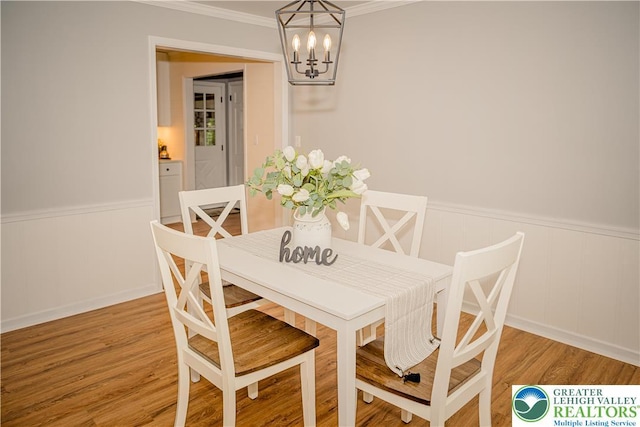 dining room with a chandelier, a wainscoted wall, crown molding, and wood finished floors