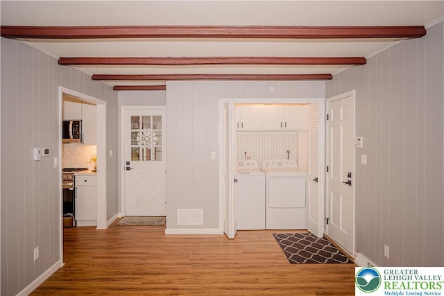foyer entrance featuring washing machine and dryer, beam ceiling, light wood-style floors, and wood walls
