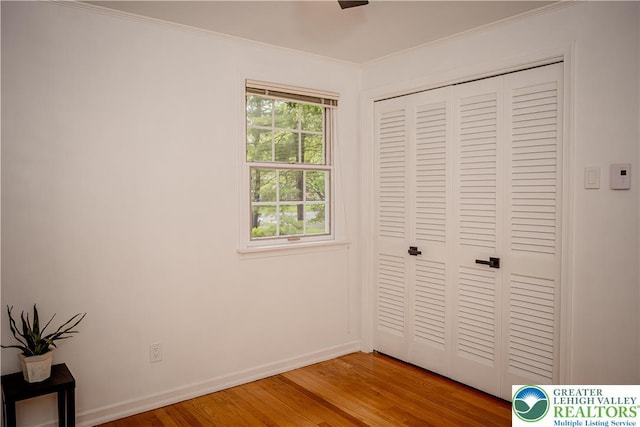 unfurnished bedroom featuring light wood-type flooring, ornamental molding, baseboards, and a closet