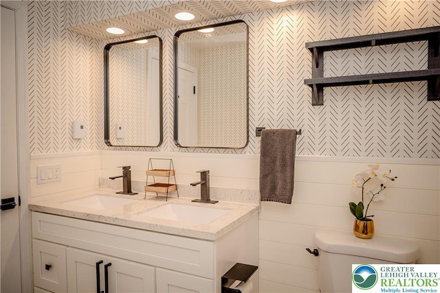 bathroom with wallpapered walls, toilet, and double vanity