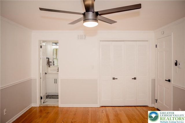 unfurnished bedroom with wood finished floors, ornamental molding, a closet, connected bathroom, and ceiling fan