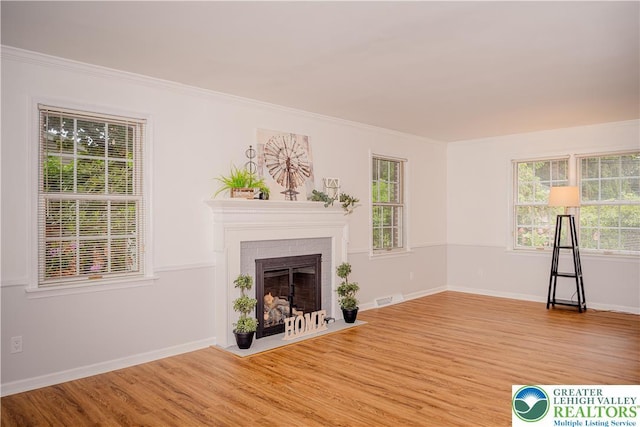 unfurnished living room with wood finished floors, a brick fireplace, crown molding, and baseboards