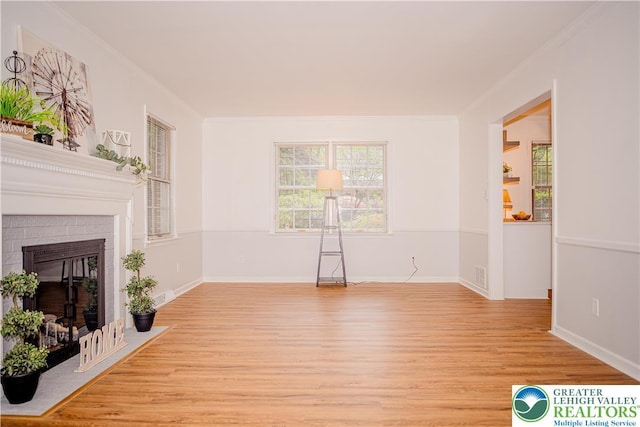 unfurnished living room featuring light wood finished floors, crown molding, a brick fireplace, and baseboards