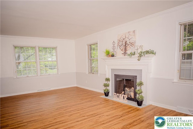 unfurnished living room with ornamental molding, wood finished floors, healthy amount of natural light, a tiled fireplace, and baseboards
