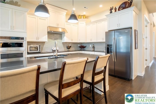 kitchen featuring stainless steel appliances, dark wood-style flooring, under cabinet range hood, backsplash, and hanging light fixtures