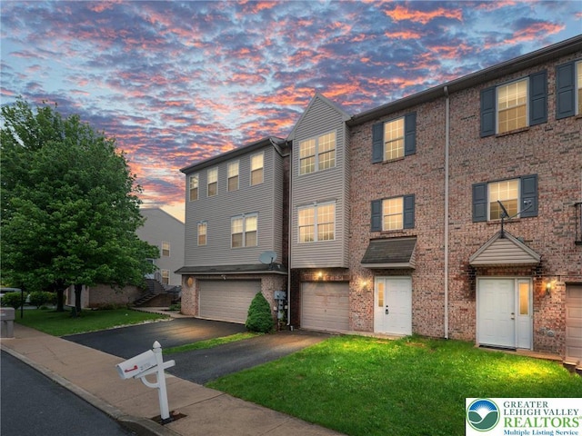 townhome / multi-family property with driveway, a garage, brick siding, and a lawn