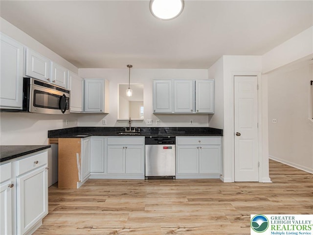 kitchen featuring stainless steel appliances, a sink, light wood-style floors, and dark countertops