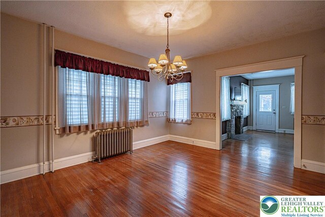 603 S Main St, Bangor Borough, PA 18013 - empty room with radiator, a chandelier, wood finished floors, a fireplace, and plenty of natural light