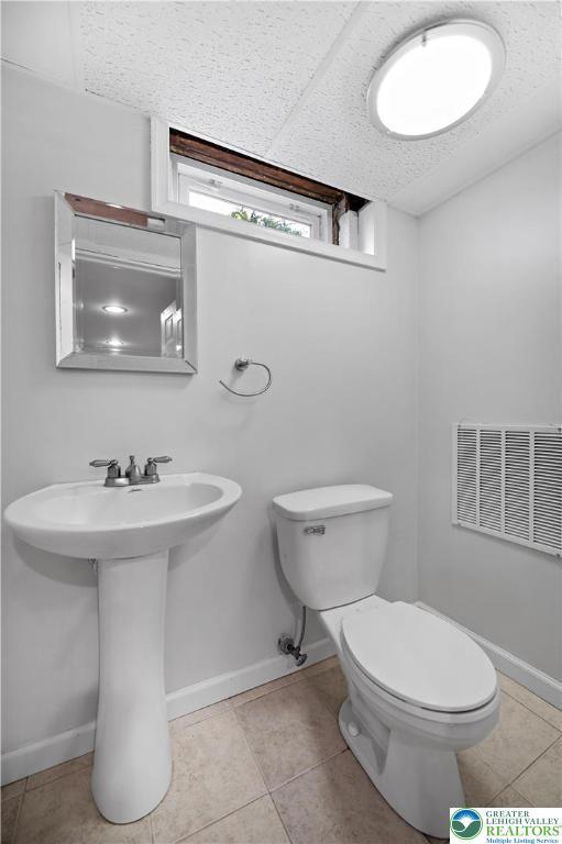 half bath featuring toilet, tile patterned floors, baseboards, and a sink