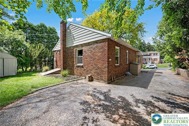 view of property exterior featuring a chimney, brick siding, a storage unit, an outbuilding, and a yard